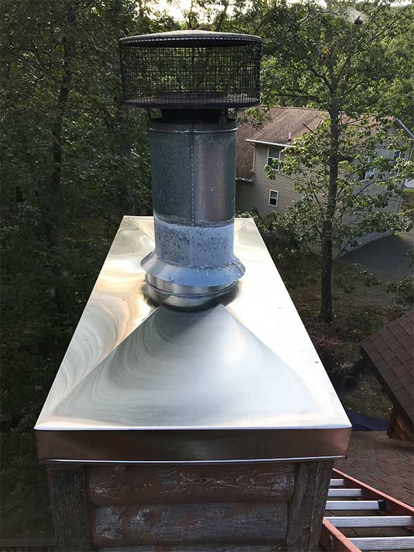 Stainless steel chimney chase cover on masonry chimney - two story home and trees in the background