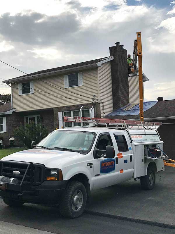 Service Truck in Driveway of two story home with tech on a lift repairing chimney - Lackawanna County PA - Integrity Chimney Service
