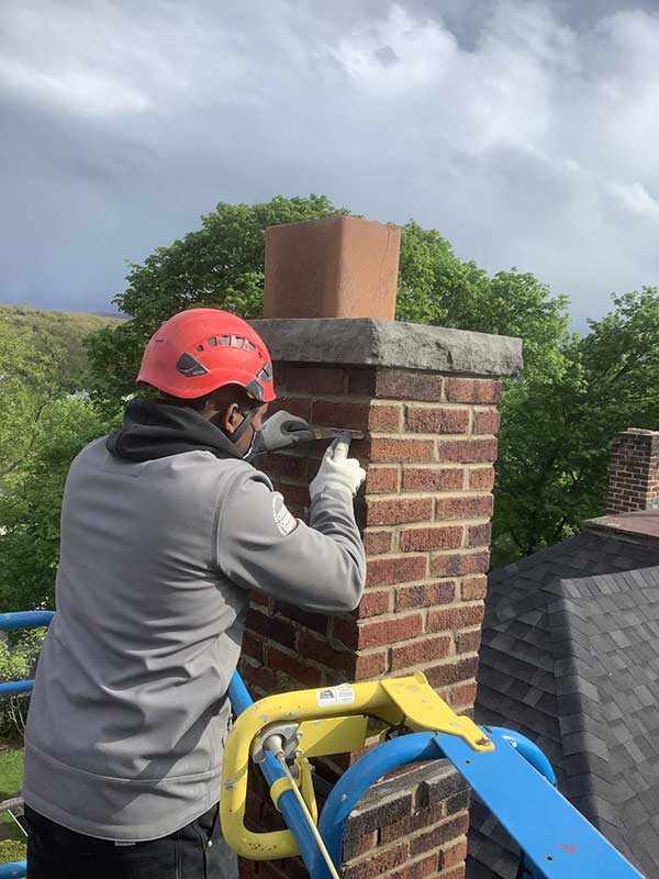Chimney Tech Repairing Chimney on scaffolding with trees and clouds in background - Lackawanna County PA - Integrity Chimney Service