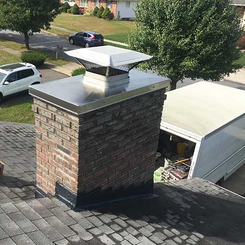 Masonry Chimney & Chase Cover Atop Roof with a white and a black car and a work truck in the background
