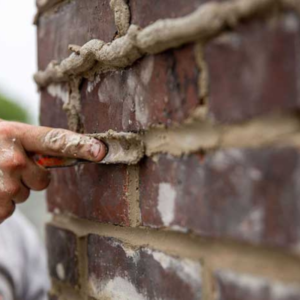 A shot of a hand using a scraping tool to smooth out mortar joints on brickwork