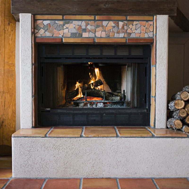 a fireplace with a partial tile facing next to a nicely stacked pile of logs